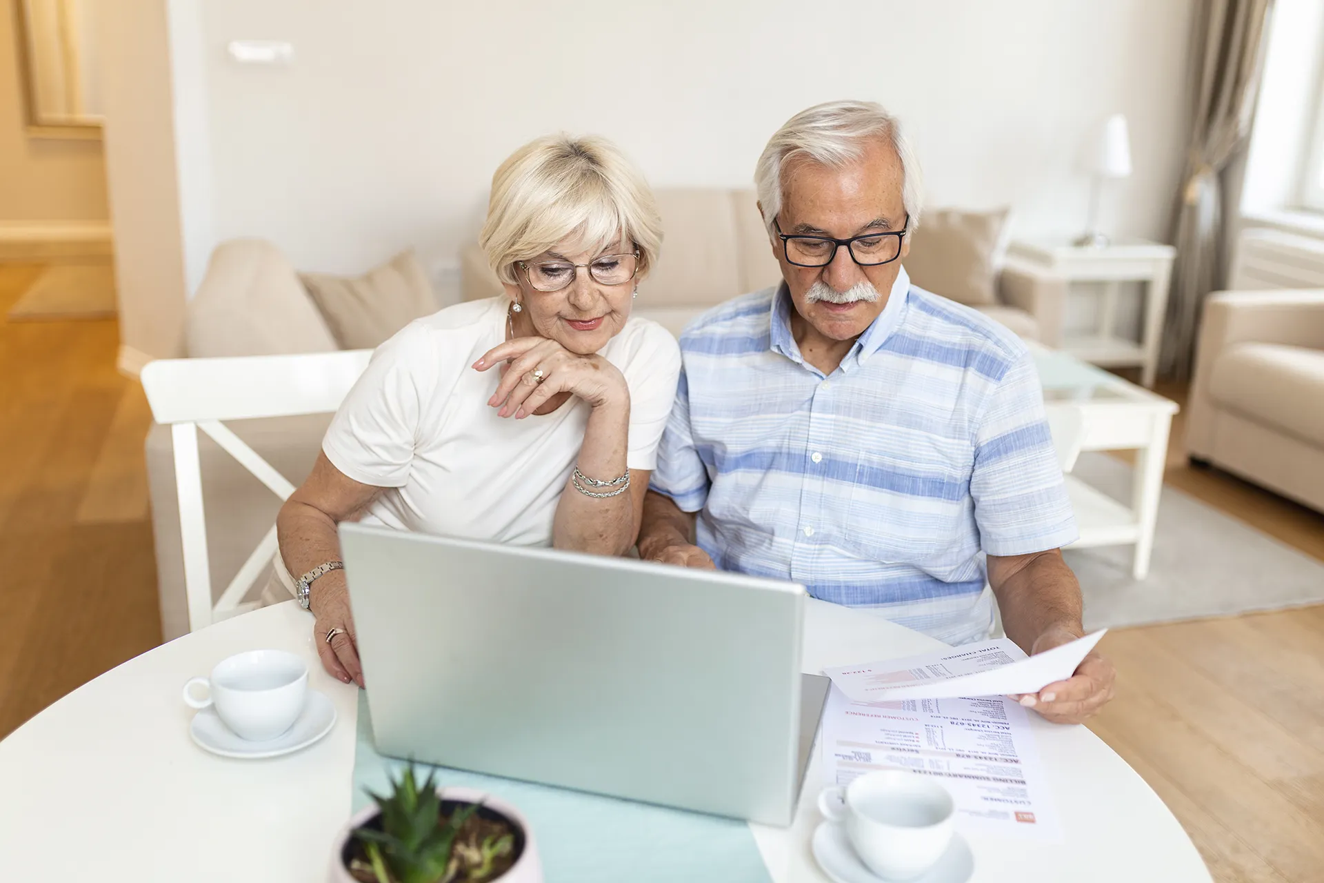 Senior couple reviewing financial documents on a laptop while discussing their investment portfolio and retirement goals.